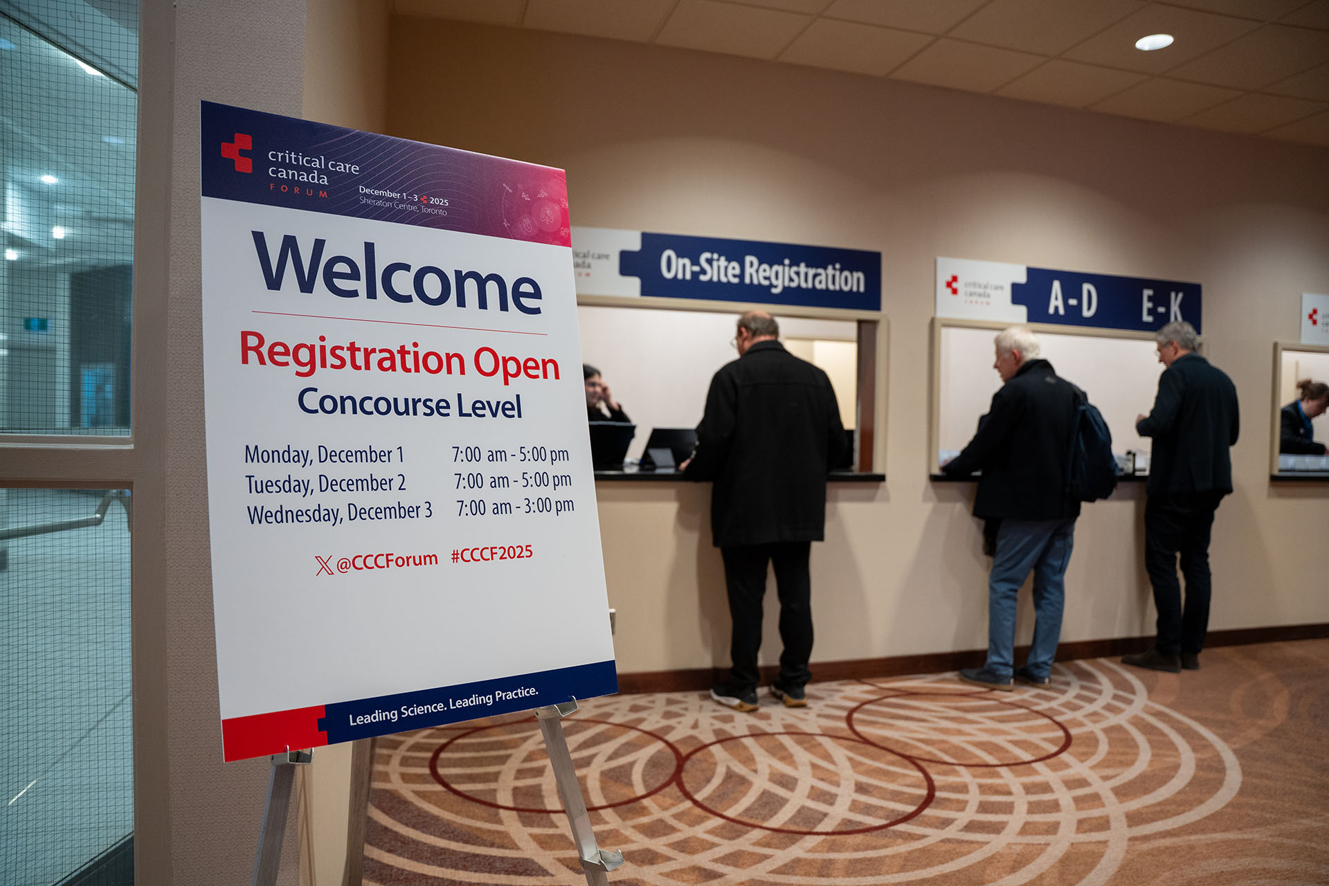 registration sign on metal stand with people at on-site registration desks in beige room