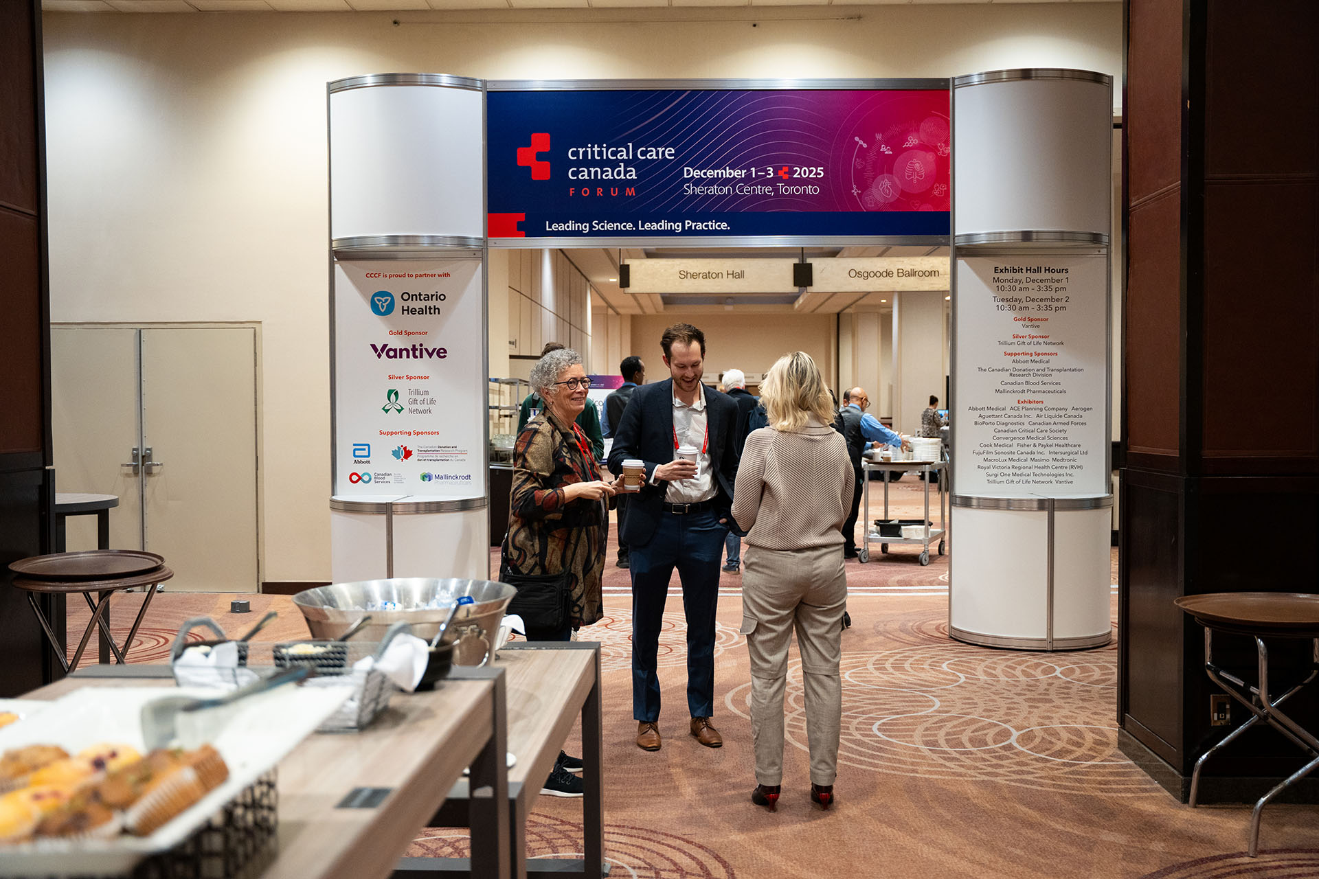 conference entrance with metal and plastic signage in blue and red, people standing on carpeted floor