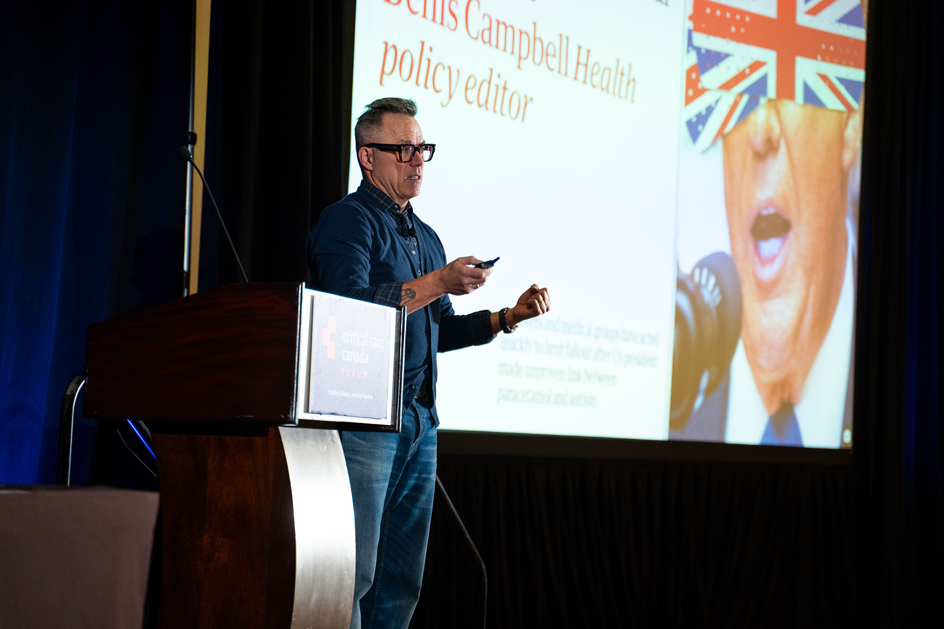man giving presentation with wooden podium and large white screen with colorful projection