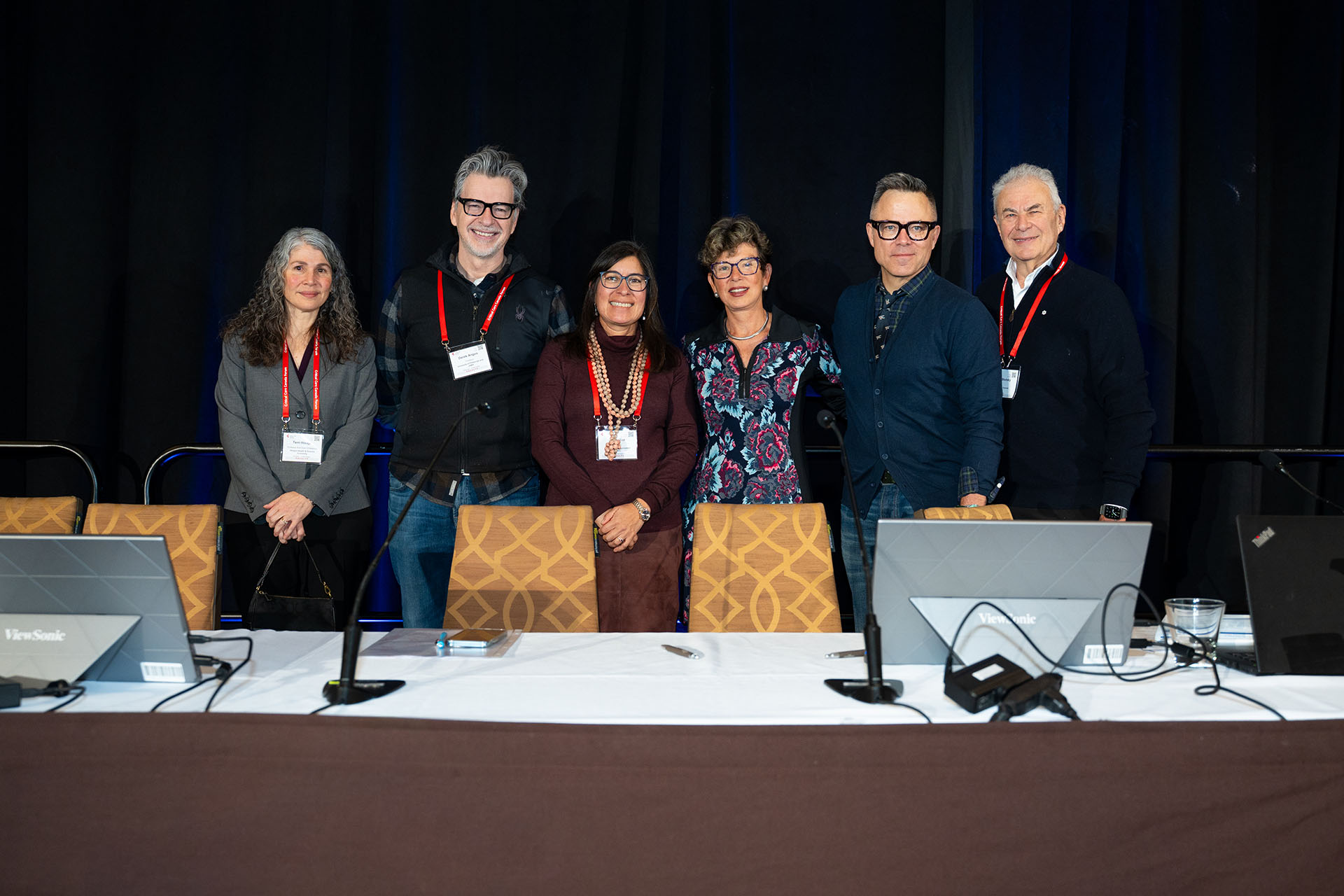 Group of six people standing behind wooden chairs with patterned fabric at a conference table