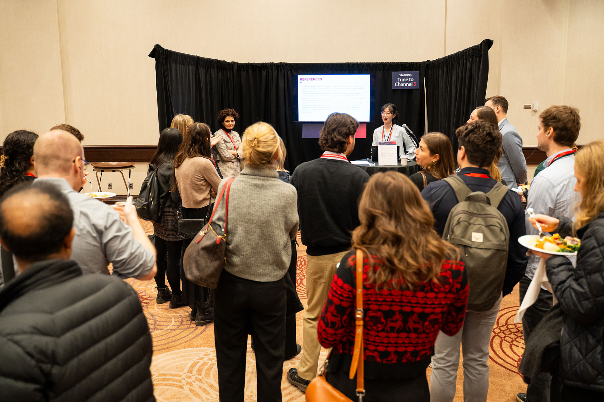Group of people attending a presentation with a black fabric backdrop and a digital screen in beige room